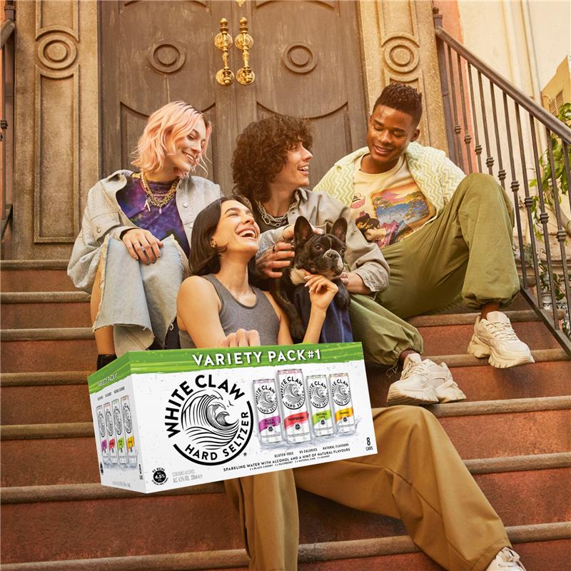 Group of friends sitting on steps with a box of White Claw hard seltzer Variety Pack.